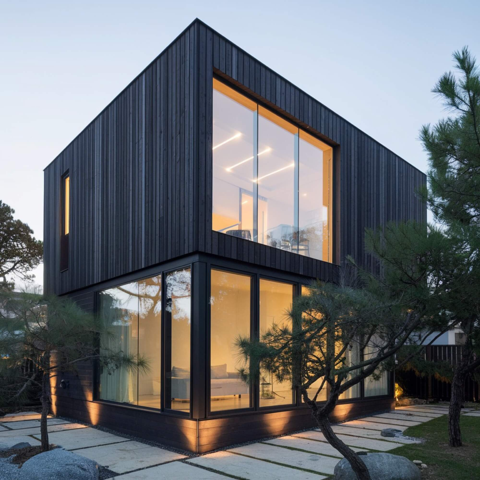 En arkitektritad villa med svart stående träpanel och stora fönsterpartier, ett exempel på modern nybyggnation.