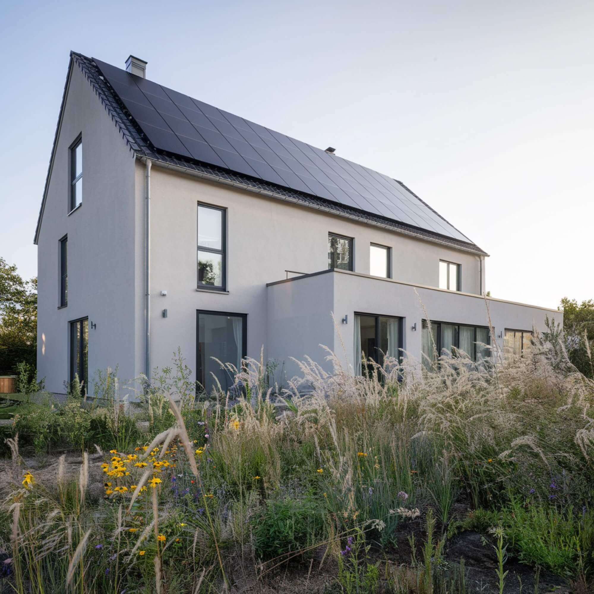 En modern, ljusputsad villa med integrerade solceller på taket, en hållbar lösning för nybyggnation.